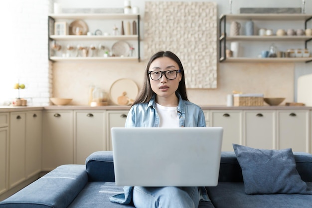 Porträt einer jungen schönen asiatischen Bloggerin, die zu Hause auf der Couch sitzt und ein Weiß hält