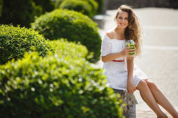 Porträt einer jungen schönen attraktiven Frau draußen im Sommer mit einem Glas eiskaltem Saft oder Getränk. Hübsches Mädchen draußen mit frischem Mojito