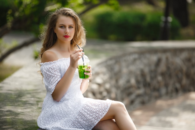 Porträt einer jungen schönen attraktiven Frau draußen im Sommer mit einem Glas eiskaltem Saft oder Getränk. Hübsches Mädchen draußen mit frischem Mojito