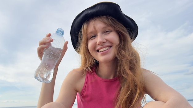 Porträt einer jungen schönen Frau, die an einem Sommertag Mineralwasser aus einer Plastikflasche trinkt