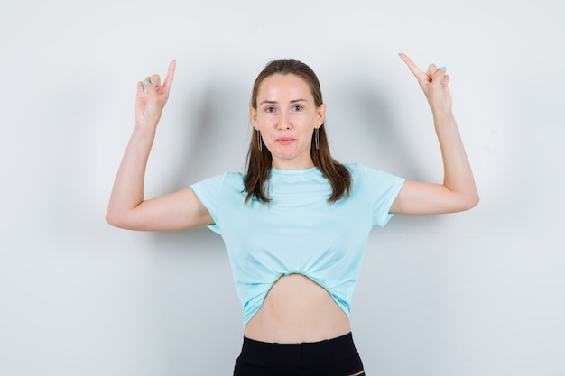 Porträt einer jungen schönen Frau, die im T-Shirt nach oben zeigt und selbstbewusste Vorderansicht schaut