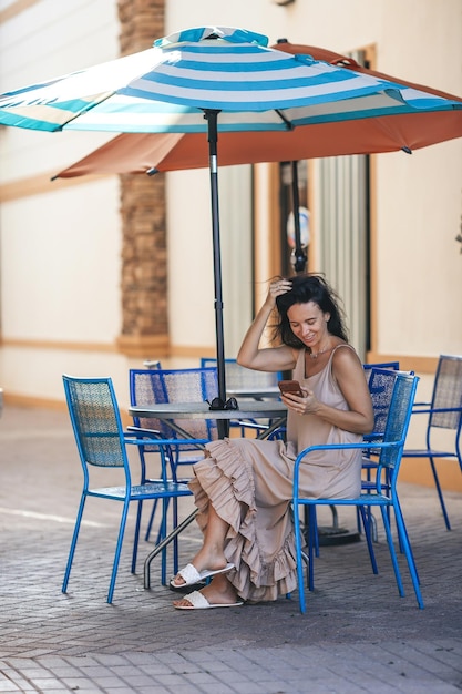 Porträt einer jungen schönen Frau, die in einem Café im Freien sitzt, ein glücklicher Tourist in einem Restaurant im Freien mit ihrem Smartphone