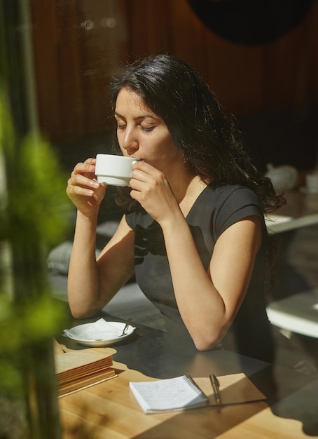 Porträt einer jungen schönen Frau, die in einem Café im Freien sitzt und Kaffee trinkt