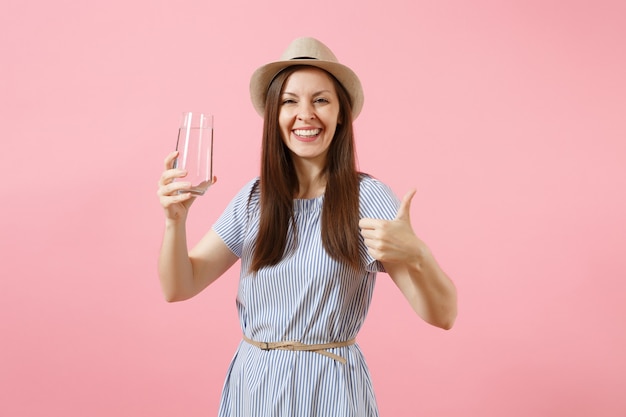 Porträt einer jungen schönen Frau in blauem Kleid, Hut, die klares frisches reines Wasser aus Glas hält und trinkt, isoliert auf rosafarbenem Hintergrund. Gesunder Lebensstil, Menschen, Konzept der aufrichtigen Emotionen. Platz kopieren