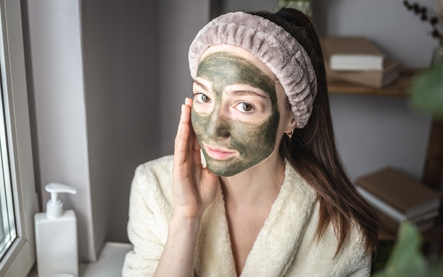 Porträt einer jungen schönen frau in einem bademantel und mit einer kosmetischen grünen maske im gesicht