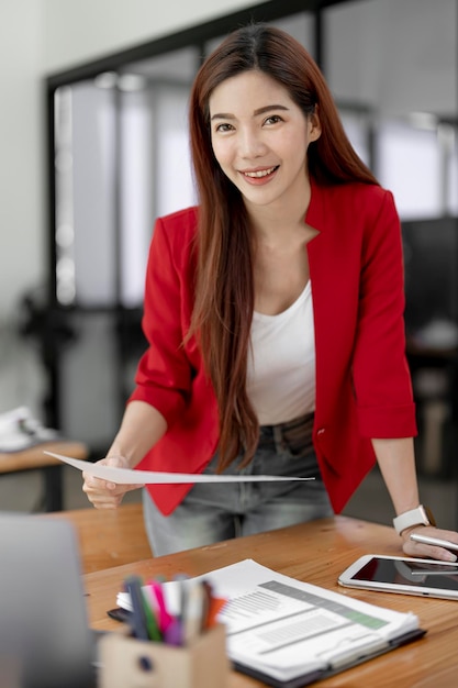 Porträt einer jungen Smiley-Geschäftsfrau, die Papierkram hält, der an ihrem Schreibtisch steht