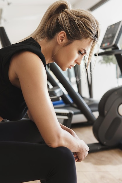 Porträt einer jungen sportlichen Frau in schwarzer Sportbekleidung, die sich nach ihrem Fitnesstraining im modernen Fitnessstudio ausruht