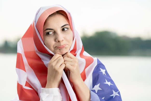 Porträt einer jungen traurigen Flüchtlingsfrau mit US-Nationalflagge auf Kopf und Schultern. Einwanderung in das Konzept der Vereinigten Staaten.