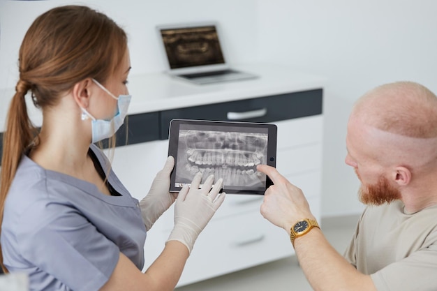 Porträt einer jungen Zahnärztin, die neben einem erwachsenen Mann in der Klinik steht