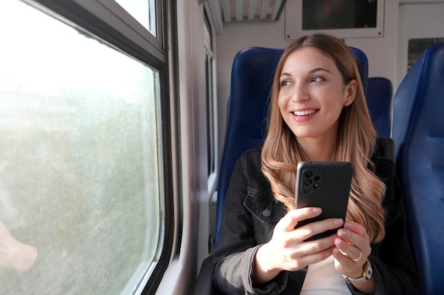 Porträt einer jungen zufriedenen Frau, die mit öffentlichen Verkehrsmitteln unterwegs ist und ein Handy sitzend und gedankenlos entspannt hält