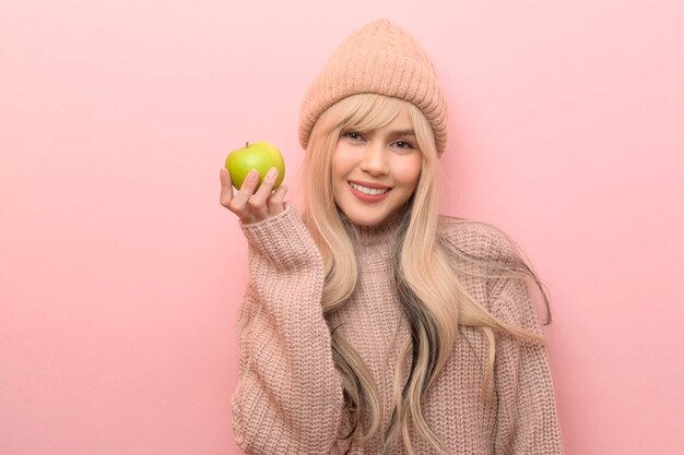 Porträt einer kaukasischen jungen Frau mit Pullover, die grünen Apfel über rosa Hintergrund hält