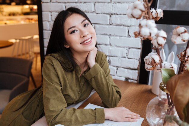 Porträt einer lächelnden asiatischen Frau, die am Café sitzt