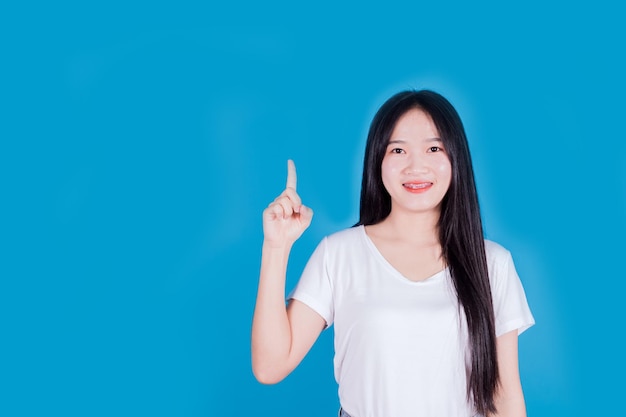 Porträt einer lächelnden asiatischen Frau, die auf blauem Hintergrund mit dem Finger zur Seite zeigt