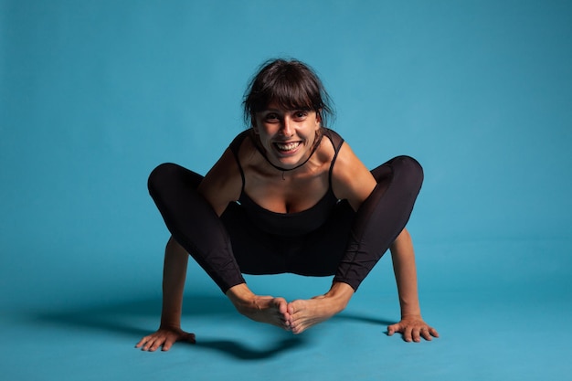 Porträt einer lächelnden athletischen erwachsenen Person, die Yoga-Position praktiziert, die mit gekreuzten Beinen in den Händen steht und einen gesunden Lebensstil verfolgt. Personal Trainer dehnt die Körpermuskulatur während des Fitnesstrainings