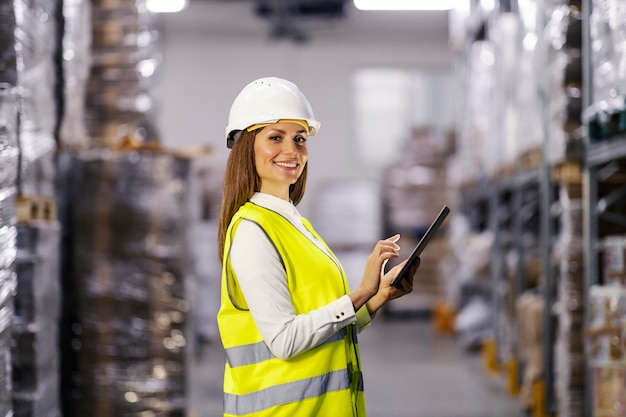 Porträt einer lächelnden Controllerin, die im Fabriklager steht und ein Tablet verwendet