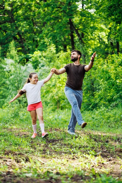 Porträt einer lächelnden Familie, die im Wald um Bäume herumgeht und Spaß hat Kleines Mädchen, das die Hand eines glücklichen Vaters hält