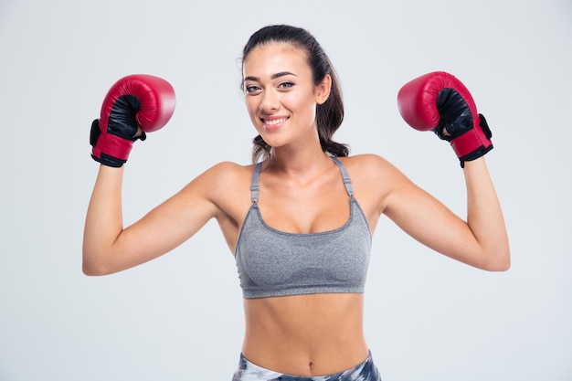 Porträt einer lächelnden Fitnessfrau, die mit Boxhandschuhen in Siegeshaltung lokalisiert auf einer weißen Wand steht