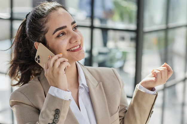 Porträt einer lächelnden Frau, die am Tisch im Büro sitzt und telefoniert