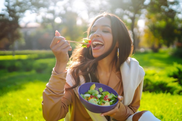 Porträt einer lächelnden Frau, die an einem sonnigen Tag Salat im Freien isst Gesundes Lebensstil Konzept Picknick