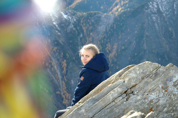 Foto porträt einer lächelnden frau, die auf einem felsen sitzt