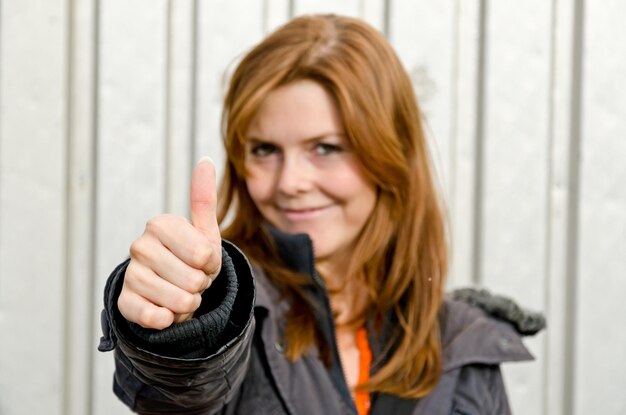 Foto porträt einer lächelnden frau, die die daumen gegen den verschluss zeigt