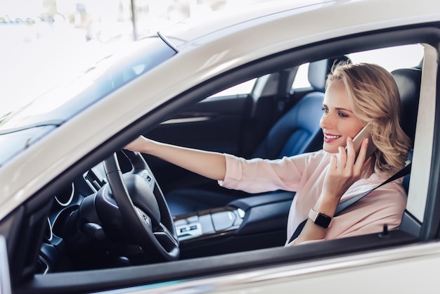 Porträt einer lächelnden Frau, die im Auto sitzt und mit dem Smartphone spricht