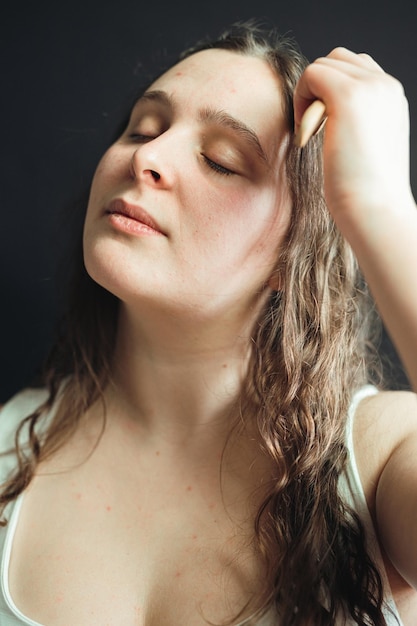 Porträt einer lächelnden Frau, die sich die Hand vors Gesicht hält und in einem Studio mit schwarzem Hintergrund posiert. Eine junge Erwachsene trägt täglich eine nährende Gesichtsmaske auf ihre Haut auf