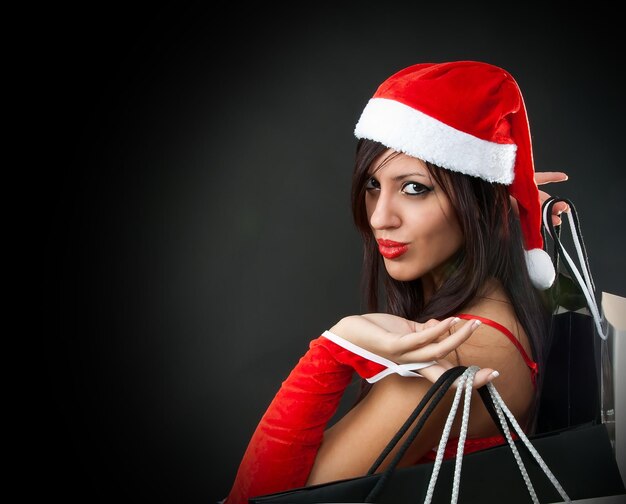 Porträt einer lächelnden Frau im Weihnachtsmannskostüm mit Einkaufstaschen auf schwarzem Hintergrund