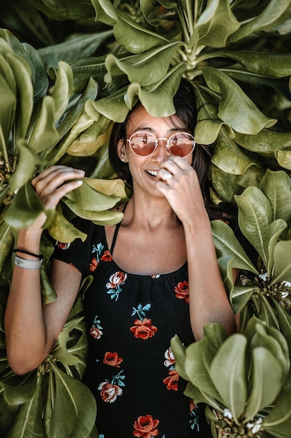 Foto porträt einer lächelnden frau in sonnenbrille, die gegen einen baum steht