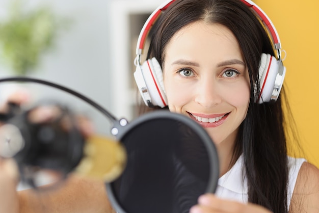 Porträt einer lächelnden Frau mit Kopfhörern vor Mikrofon im Studio