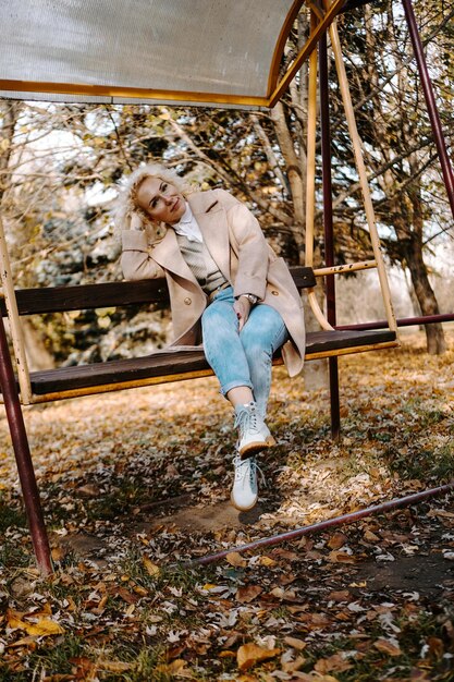 Porträt einer lächelnden Frau mittleren Alters, die im Herbstpark auf der Schaukel sitzt und schwingt