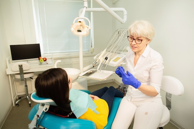 Porträt einer lächelnden Frau, sitzend am zahnmedizinischen Stuhl mit Doktor in der zahnmedizinischen Praxis