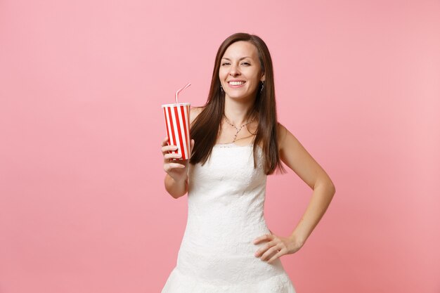 Porträt einer lächelnden, fröhlichen Frau im schönen weißen Kleid, die einen Plastikbecher mit Cola oder Soda hält und hält