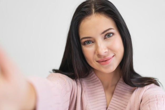 Porträt einer lächelnden, fröhlichen, hübschen asiatischen Frau, saubere, frische, gesunde weiße Haut, die lächelnd in die Kamera blickt und Live-Selfie auf dem Smartphone auf dem Bett zu Hause macht