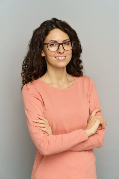 Porträt einer lächelnden Geschäftsfrau mit gefalteten Händen an der grauen Wand selbstbewusste Dame in Brillen
