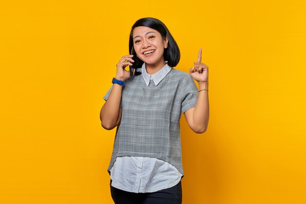 Porträt einer lächelnden jungen Asiatin, die Smartphone mit einer Idee oder Frage hält, die mit dem Finger zeigt