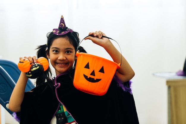 Porträt einer lächelnden jungen Asiatin im Halloween-Kostüm, die einen Eimer mit Kürbis hält