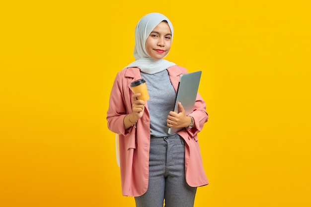 Porträt einer lächelnden jungen Asiatin mit Laptop und Kaffee auf gelbem Hintergrund isoliert