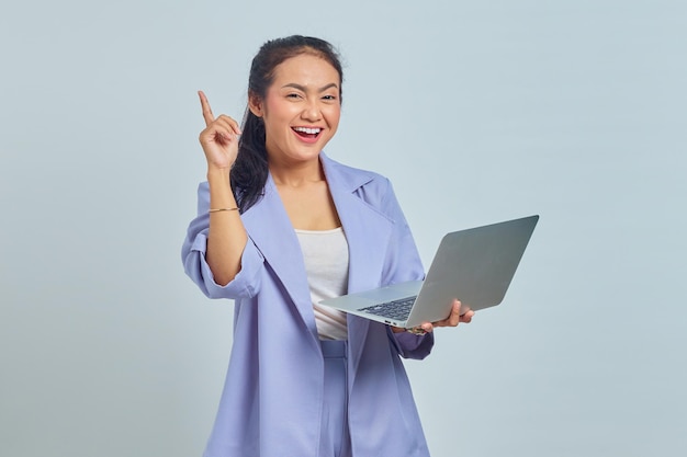 Porträt einer lächelnden jungen asiatischen Frau, die einen Laptop hält, mit dem Finger nach oben zeigt und eine Idee isoliert auf weißem Hintergrund hat