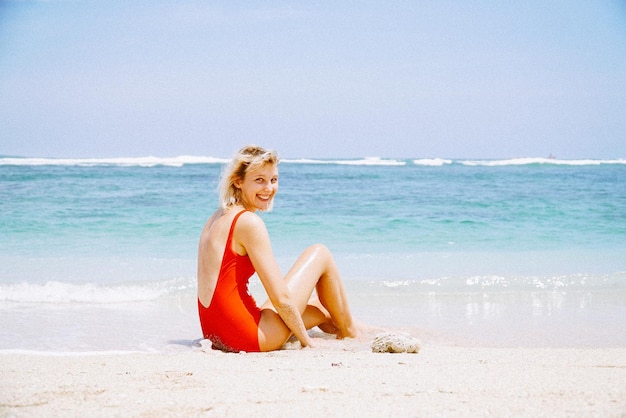 Porträt einer lächelnden jungen Frau, die am Strand gegen den Himmel sitzt
