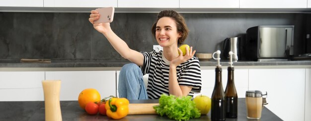 Foto porträt einer lächelnden jungen frau, die auf einem tisch sitzt und ein handy benutzt