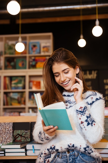 Porträt einer lächelnden jungen Frau, die ein Buch liest und auf dem Handy spricht