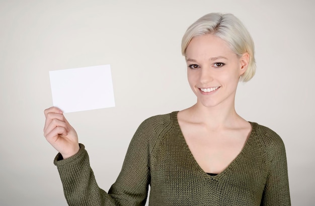 Foto porträt einer lächelnden jungen frau, die ein leeres papier in der hand hält und vor weißem hintergrund steht