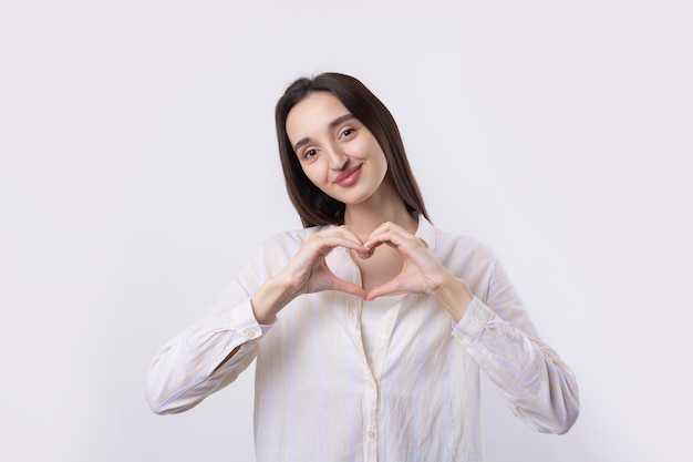 Porträt einer lächelnden jungen Frau, die Herzgeste mit ihren Fingern lokalisiert über weißem Hintergrund zeigt