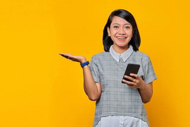 Porträt einer lächelnden jungen Frau, die Kopienraum in der Handfläche zeigt und Handy hält