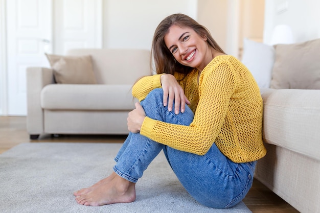 Porträt einer lächelnden jungen Frau, die sich nachmittags allein auf ihrem Wohnzimmersofa zu Hause entspannt