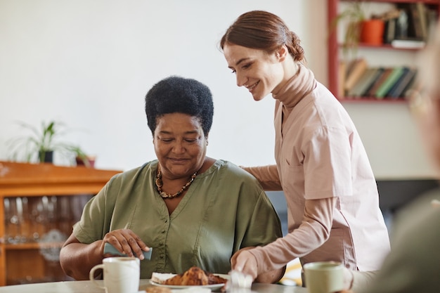 Porträt einer lächelnden jungen Frau, die sich um eine ältere afroamerikanische Dame im Pflegeheimkopierraum kümmert