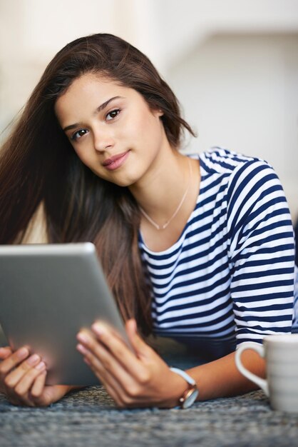 Porträt einer lächelnden jungen Frau, die zu Hause mit einem digitalen Tablet auf dem Boden liegt