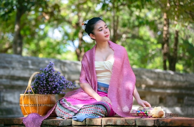 Porträt einer lächelnden jungen frau in thailändischer lanna traditional clothes, die durch blumenkorb sitzt