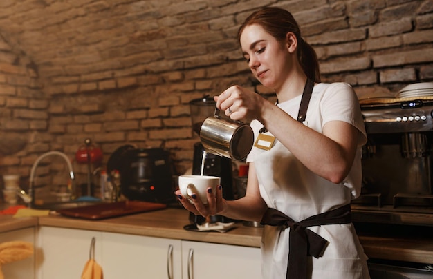 Porträt einer lächelnden jungen kaukasischen Frau, die heiße Milch im Kaffee konsumiert, eine Kellnerin hält ein Weiß